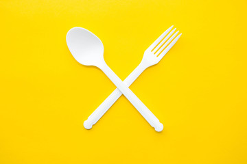 Plastic white crossed fork and spoon on on yellow background. Cooking utensil. Cutlery sign. Top view. Minimalist Style. Copy, empty space for text