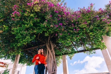 guy embraces girl from back side. couple in red sweaters near tr