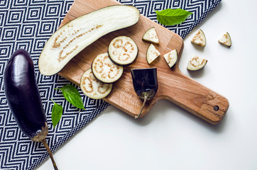 Creative layout of whole and sliced eggplants, cutting board and tablecloth.