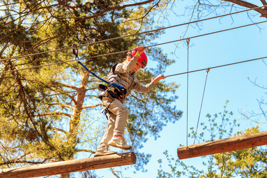 Happy school girl enjoying activity in climbing adventure park on summer day. Rope park climbing center. Hiking in rope park girl in safety equipment. Roping park. Child. Adorable little girl enjoying