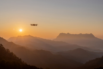 The drone with the professional camera takes pictures of the misty mountains at sunset.