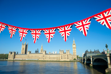 Fototapeta na wymiar String of Union Jack flag bunting hanging in front of Big Ben at the Houses of Parliament in London, UK with bright blue sky copy space