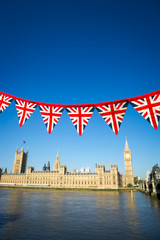 Fototapeta na wymiar String of Union Jack flag bunting hanging in front of Big Ben at the Houses of Parliament in London, UK with bright blue sky copy space