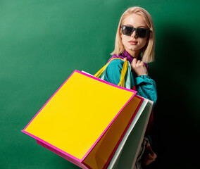 Blonde girl in 90s style jacket with shopping bags on green background