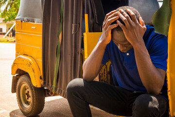 young african man looking and feeling sad sitting in a rickshaw holding his head