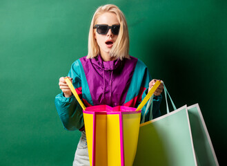 Blonde girl in 90s style jacket with shopping bags on green background