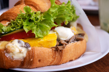 Croissant sandwiches served on wooden board. Croissants with egg, melted cheese, parsley, chicken ham, smoked salmon.