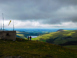 Obraz premium Deux randonneurs au sommet de la montagne dans les volcans d'Auvergne avec vue panoramique sur lac et horizon lointain, belle couche nuageuse grise