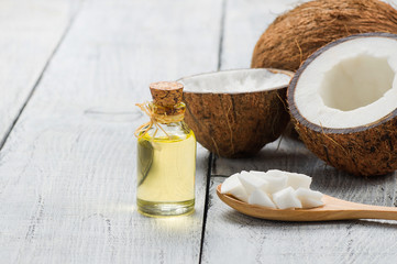 Glass bottle of coconut oil with fresh coconut fruit on wooden rustic background, alternative theraphy medicine concept, Cocos nucifera