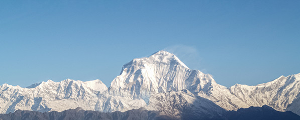 Mountain landscape panorama. Majestic mountain peaks covered with snow against a bright blue sky.