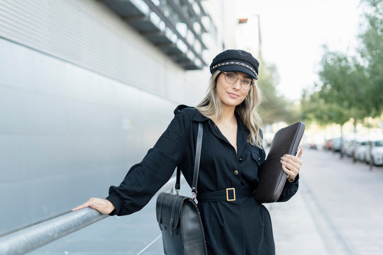 Young blond businesswoman wearing black sailor's cap and holding laptop bag