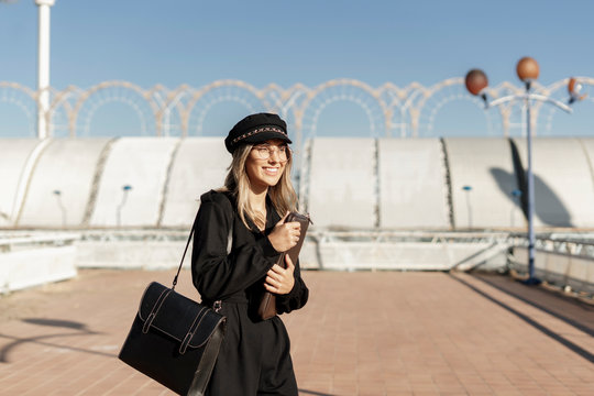 Young blond businesswoman wearing black sailor's cap and holding laptop bag