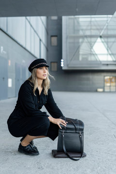 Young blond businesswoman wearing sailor's cap and searching in her bag