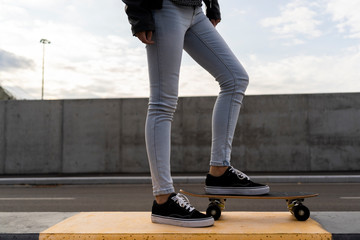 Legs of woman with skateboard standing on bollard
