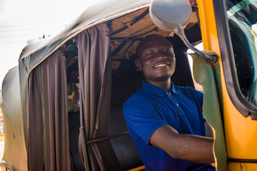 young african man driving a tuk tuk taxi smiling on a very sunny day