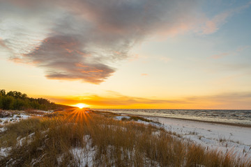Seaside with sand dunes with snow and colorful sky at sunset, sunrise