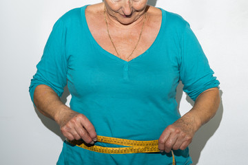older woman body measuring her belly with yellow tape measure