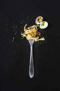 High angle view of clams and noodles in fork on black background