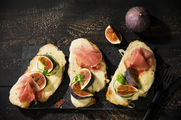 High angle view of baked cheese bread with fig slices and ham served on wooden table