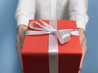 A young man in a white shirt gives a gift a blue background. Red gift box with white ribbon. Concept of holidays. Close up. Man 4k stock footage
