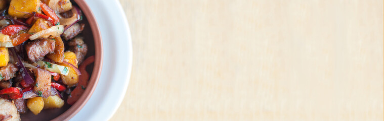 Roasted pork with steamed vegetables: potato, onion, bell pepper in the ceramic plate. Caucasian georgian food ojahuri. Horizontal top view from above.