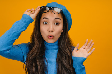 Close up photo of cute girl in eyewear wearing blue sweater and beret isolated over yellow...