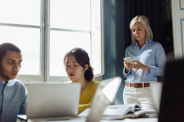 Colleagues discussing project, while mature woman is using smartphone in background