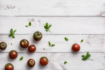 Naklejka na ściany i meble Ripe black prince tomatoes and basil leaves on white wooden background. Top view, flat lay, copy space