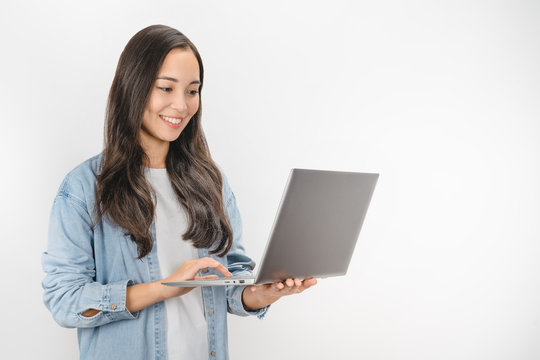 Young happy smiling woman in casual clothes holding laptop and sending email standing over white background