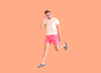 Fototapeta na wymiar Jumping young man in beachwear on color background