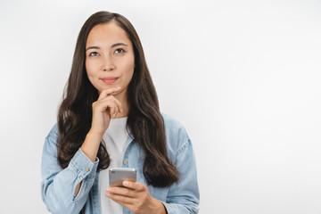 Image of dreaming young beautiful asian woman posing over white wall background and using mobile phone