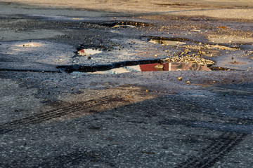 Pits on the road. Close-up photograph of a part of the road, asphalt on which there are many pits in which rainwater is poured