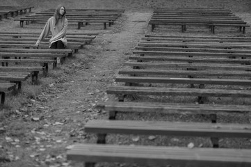 Obraz premium Sad depressed girl sitting alone on bench in park with multiple desolate benches around her. Loneliness and despair concept.