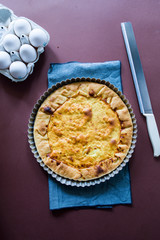 Quiche with.egg, cream, scamorza cheese and spec ham, round shaped on an aluminium mold, top view on a dark brown background