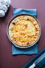 Quiche with.egg, cream, scamorza cheese and spec ham, round shaped on an aluminium mold, top view on a dark brown background