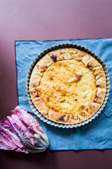 Quiche with.egg, cream, scamorza cheese and spec ham, round shaped on an aluminium mold, top view on a dark brown background