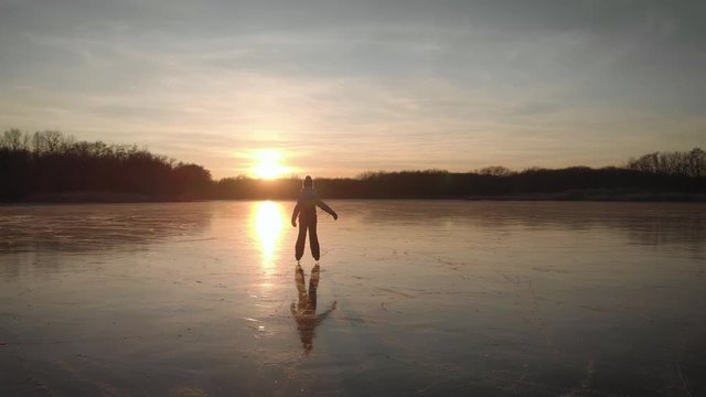 Cute little girl is going skate outdoors at sunset. A schoolgirl enjoying ice skating at frozen lake in winter season. Winter sports.