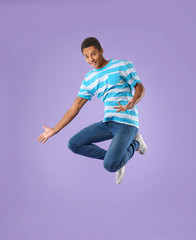 Jumping African-American teenager boy on color background