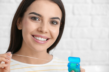 Beautiful young woman with dental floss on light background