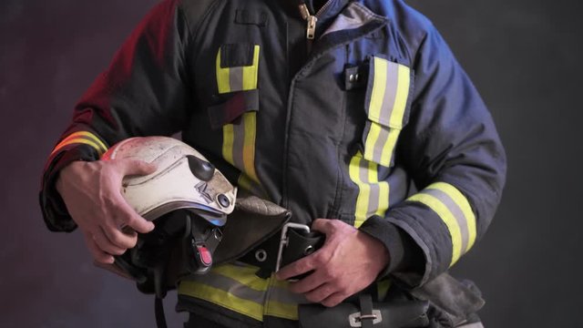 Close-up view of a brave firefighter in special uniform holds protective helmet standing against a gray wall