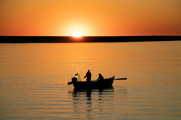 Naklejka na ściany i meble Fishermen in rowing boat at sunset in Douro River estuary, Porto, Portugal. Golden hour