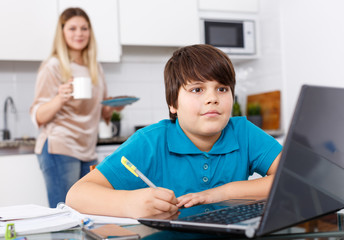 Boy doing homework, mother cooking