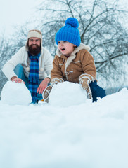 Thanksgiving day and Christmas. Cute little child boy and happy father on snowy field outdoor. Happy father and son making snowman in the snow.