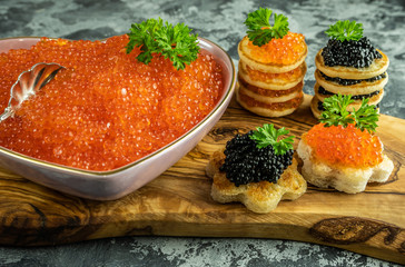 Red caviar in a plate in the form of a heart with pancakes and toasts