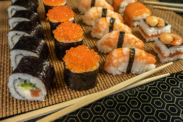 Sushi and rolls with red caviar and shrimp on a bamboo mat with food sticks