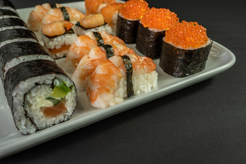 Sushi and rolls with red caviar and shrimp on a white dish