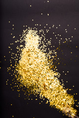 Creative photo of  golden confetti on black background coming out of a plastic container. . Flat lay of christmas, anniversary, new year celebration minimal party concept.