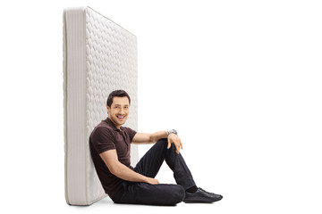 Young guy sitting on the floor and leaning against a bed mattress