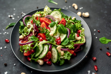 Salad with pomegranate, tomatoes, fresh cucumbers, onions, sesame seeds and cashew nuts, spices on a stone background. Healthy vegetarian food.