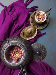 A cup of Rose tea with a metal tea pot.